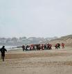 A group of migrants walks on the beach with an inflatable dinghy, to leave the coast of northern France and to cross the English Channel, in Wimereux near Calais, France, December 16, 2021. REUTERS/Stephane Mahe