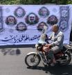 TOPSHOT - A man rides his motorcycle past a poster displaying the portraits of Iranian military generals and nuclear scientists, killed in Israel's attack early on June 13, in Tehran on June 14, 2025. Israel's military said that its fighter jets were set to resume striking targets in Tehran, after announcing it had hit air defences in the Iranian capital area overnight, as Israel and Iran trade fire with such intensity for the first time following decades of enmity and conflict by proxy, with fears of a prolonged conflict engulfing the region. (Photo by Atta KENARE / AFP)