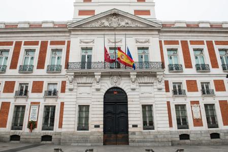 Fachada de la Real Casa de Correos, sede de la Comunidad de Madrid, con las banderas a medio asta durante el minuto de silencio en el primer día del luto oficial por los fallecidos del COVID-19 decretado por la presidenta madrileña, Isabel Díaz Ayuso, en Madrid (España) a 30 de marzo de 2020.