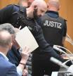 One of nine suspected participants in a coup plot wears handcuffs and hides his face behind a folder as he is brought to the courtroom to take the stand in the first set of proceedings in Stuttgart, southern Germany, on April 29, 2024. The first members of a far-right group that allegedly plotted to attack the German parliament and overthrow the government went on trial. The suspects are accused of having participated in the 