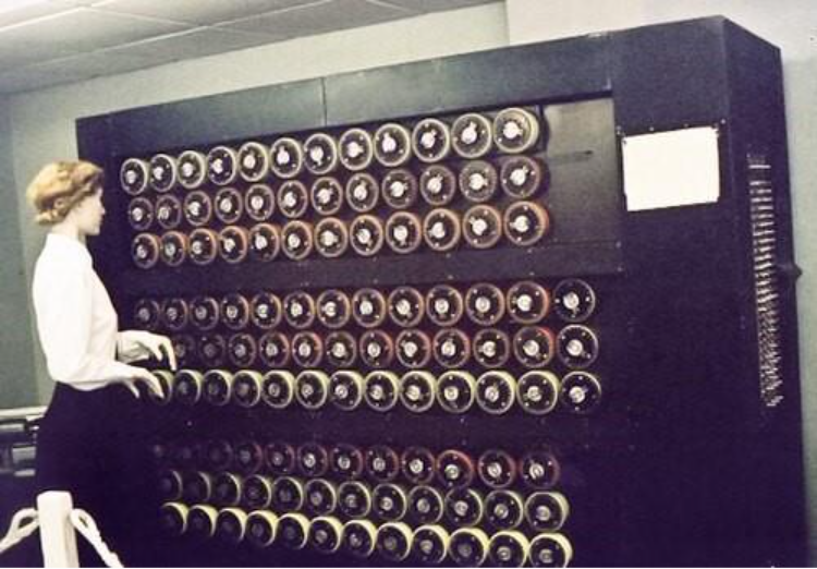 una fotografía coloreada de Bombe. En la imagen se aprecia una mujer vigilando la máquina. 