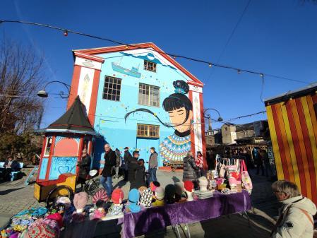 Puesto de venta de gorros junto a una casa con mural en Christiania, el barrio hippy de Copenhague 